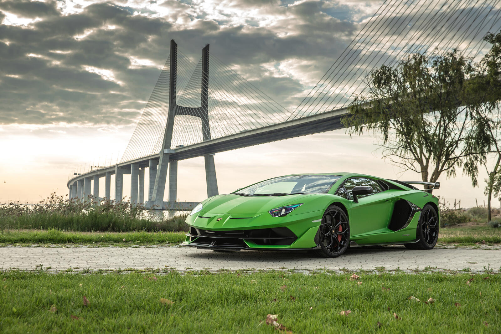 Бесплатное фото Зеленая SVJ Lamborghini Aventador на фоне моста