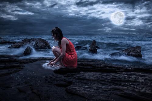 A girl in a red dress sits on the ocean at night