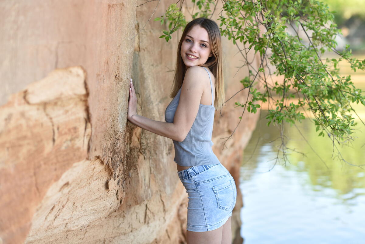 Девушка в коротких джинсовых шортах стоит у стены